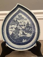 Front view of antique Chinese leaf-shaped dish showing full blue and white landscape decoration with houses, boat, pagoda, trees and bridge.