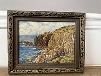 Frontal view of the framed oil on board painting depicting rocky cliffs and ocean at Lands End, England.