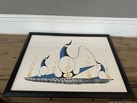 Framed lithograph print showing a stylized First Nations design in blue, beige and black with golden vertical strokes, framed in black with beige matting on wooden floor