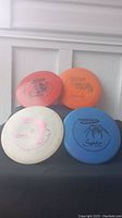Four disc golf frisbees arranged front-facing showing brand and design details on each, colors red, orange, white, and blue.