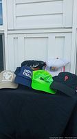 Six assorted ball caps arranged on black surface in front of white wall showing logos and color variety