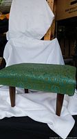 Side view of vintage footstool showing green patterned fabric upholstery and dark wooden legs.