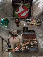 Wide view showing Stay Puft Marshmallow Man figure, three Ghostbusters figures, green ghost figure, and two separate packaging cards with Ghostbusters logo and character artwork.