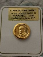 Close-up image of one limited edition 24K gold Pope John Paul II charm mounted on a white display card with gold foil label.