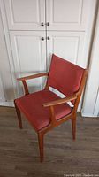Front and side view of mid-century modern armchair showing wooden frame and reddish-orange fabric upholstery.