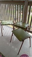 Four vintage padded stools with tubular metal frames and green colored seats. One stool has floral fabric, others have green vinyl seats worn with usage.