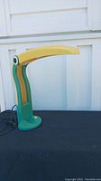Full view of pelican shaped desk lamp showing green base and neck with yellow beak and on/off button
