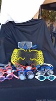 Photo showing all swimming goggles and hand paddles displayed on a black cloth backdrop, highlighting color variety and condition.