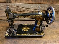 Black Singer treadle sewing machine with ornate gold decals and large metal handwheel on right.