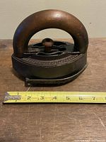Side view of the antique cast iron SAD iron with wooden handle next to a measuring tape showing 7 inches long.