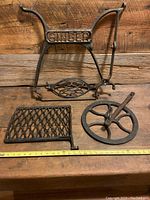 Top view of three antique Singer sewing machine treadle parts: base, foot pedal, and wheel on wooden surface with measuring tape