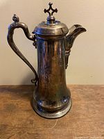 Front view of the antique Reed & Barton silver plate chalice showing the handle, spout, lid with finial, and tarnished surface.