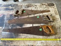 Three antique hand saws placed horizontally on a worn workbench, showing overall condition and damage.