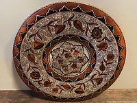 Full view of the decorated round copper plate showing detailed hand-engraved bird and floral patterns with white inlay and geometric border.