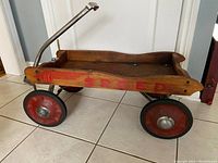 Left side view of vintage wooden wagon with red 'SPEED' and metal handle on tiled floor.