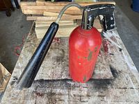 Side view of Vintage Kidde fire extinguisher showing red cylinder and black nozzle with worn paint on a workbench.