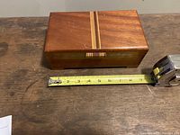 Top view of a closed mid-century modern mahogany jewelry box with decorative inlaid wood stripe, measuring about 8 14/16 inches long, shown with measuring tape for scale.