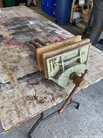 Side angled view of vintage Record bench vice showing wooden jaws and metal base with crank handle on stained workbench.