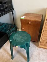 Wood cabinet with drawer and lower cabinet door, showing scratches on surface, captured from frontal angle next to green plastic stool.