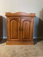 Front view of the wood cabinet with closed double doors, curved top rail with fold-down lip visible.