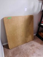 Square wooden foldable card table leaning against wall with visible scratches on surface