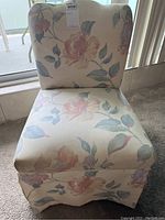 Front view of a cushioned low-height chair upholstered in fabric with a pastel floral pattern.