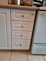 Four white drawers containing kitchen utensils and cutlery, installed under countertop near stove.