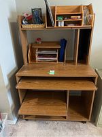 Front view of wood laminate computer desk with upper shelving and compartments, sliding keyboard tray, bottom shelf, and caster wheels.