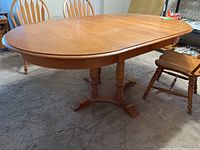 Photo of wooden pedestal dining table with oval top, supported by a single pedestal base with four feet, with two leaves inserted, showing overall condition and wear on the tabletop.