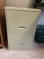Front view of a beige two drawer metal filing cabinet showing drawer handles and lock.