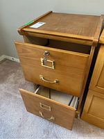 File cabinet showing two drawers, one partially opened with lock and key attached, light wood finish.