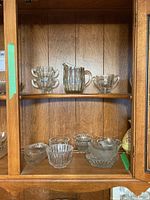 Glassware set displayed on wooden shelves including pitcher, sugar bowls, creamer and various small bowls and dishes