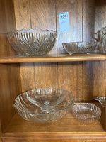 Glassware set displayed on wooden shelving showing four glass bowls and one dish with decorative pressed and cut patterns.