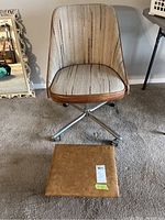 Front view of striped fabric mid-century modern swivel chair with brown vinyl trim and metal base with wheels; vinyl cushioned footstool placed on floor in front