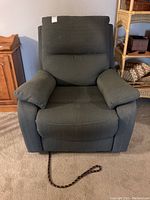 Front view of green fabric covered recliner rocker chair with rope on floor in front facing camera.