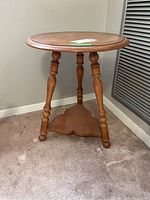 Front angle photo showing the round wooden side table with three turned legs and a lower triangular shelf.