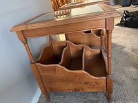 Side view of wood side table showing beveled glass top, turned legs, and magazine rack bottom with three compartments.