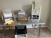 Overall view of various storage baskets and racks laid on a table including metal wire racks and plastic and wood organizers.