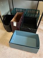 Seven assorted storage containers visible: two green plastic milk crate style boxes, one black woven basket with handle, two faux leather containers, and two paper boxes with lids partly shown.