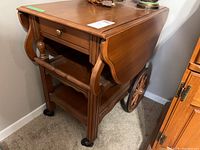 Full view of wood tea cart with one drop leaf down, showing the drawer and wheels.