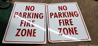 Front side of two metal rectangular signs, white background with red text 'NO PARKING FIRE ZONE'.