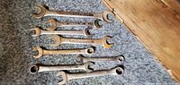 Eight open-end and box-end automotive wrenches laid on carpet showing condition and wear.