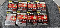 Eight Phillips halogen flood light bulbs in sealed packaging laid out in two rows of four on a gray carpeted surface.