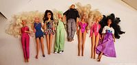 Full view of all 8 dolls including 7 female Barbies and 1 male Ken doll laid out showing hair, outfits and condition.