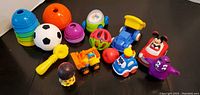 Photo showing 13 assorted kids toys including stacking cups, balls, various vehicles and character toys on a table.