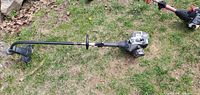 Full length view of grey Craftsman gas-powered weed eater trimmer laying on grass, showing straight shaft and trimmer head.
