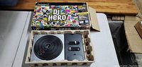 DJ Hero turntable controller in original cardboard insert with colorful DJ Hero box opened and displayed behind.