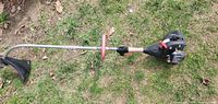 Side view of the weed eater placed on grass showing the engine, handle, and shaft with the black debris guard.