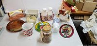 Overview of assorted collectibles and decorative items on a table including ceramics, glass jars, salt and pepper shakers, and holiday decor.