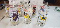 Photo showing 7 McDonald's collectible glasses with various characters including Grimace, Ronald McDonald, Captain Crook, Birdie the Early Bird, and others.